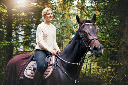 portrait of a smiling woman riding the horse against background of green leaves